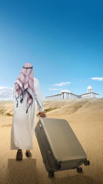 Foto vista traseira de um homem árabe vestindo keffiyeh e agal andando com uma mala para viajar no deserto