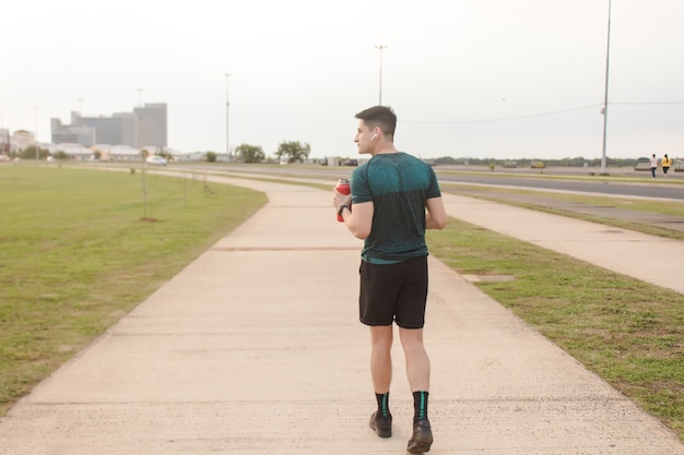 Vista traseira de um homem atlético caminhando à beira-mar enquanto bebia água.