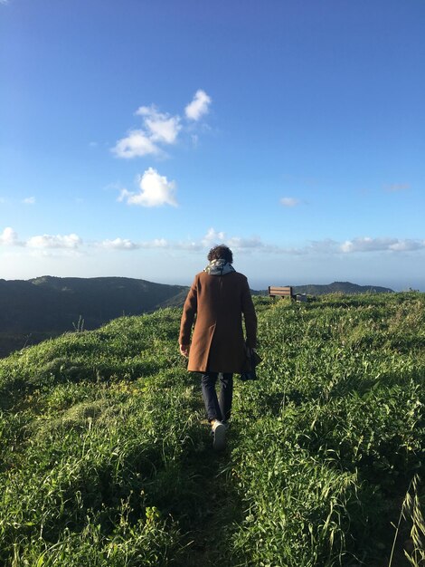 Foto vista traseira de um homem caminhando em um campo gramado contra o céu azul