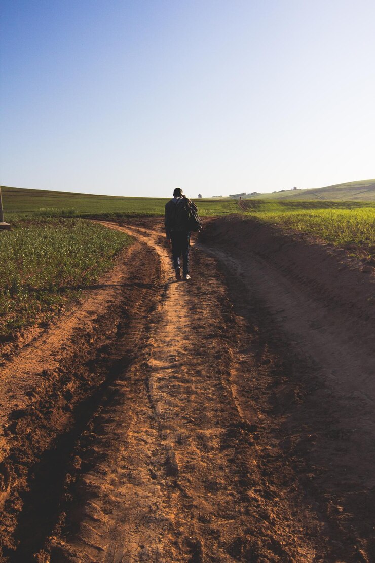Foto vista traseira de um homem caminhando em uma estrada de terra contra um céu claro