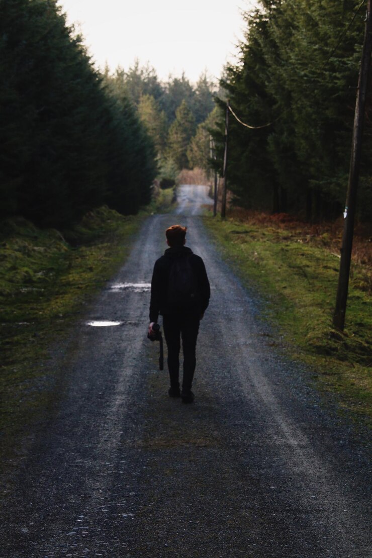 Foto vista traseira de um homem caminhando na estrada em meio a árvores
