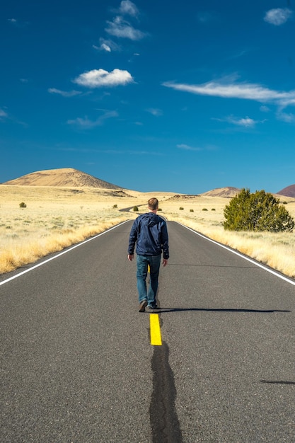 Vista traseira de um homem caminhando na estrada em meio a um campo contra o céu