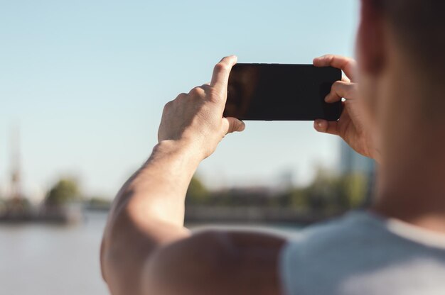 Vista traseira de um homem caucasiano parado em uma ponte tirando uma foto da cidade