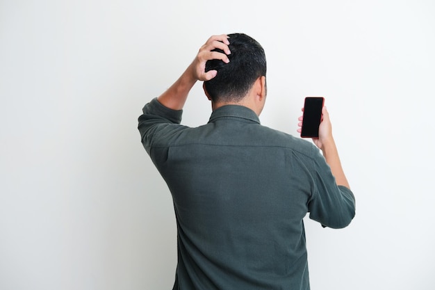 Vista traseira de um homem coçando a cabeça enquanto olha para seu handphone