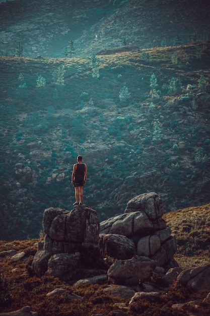 Foto vista traseira de um homem de pé em um penhasco contra montanhas
