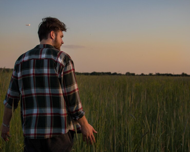 Foto vista traseira de um homem de pé em uma fazenda contra o céu durante o pôr do sol