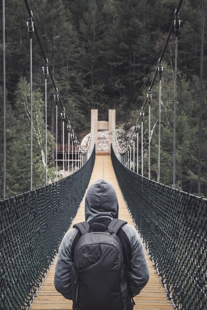 Foto vista traseira de um homem de pé em uma ponte pedonal no meio de árvores na floresta