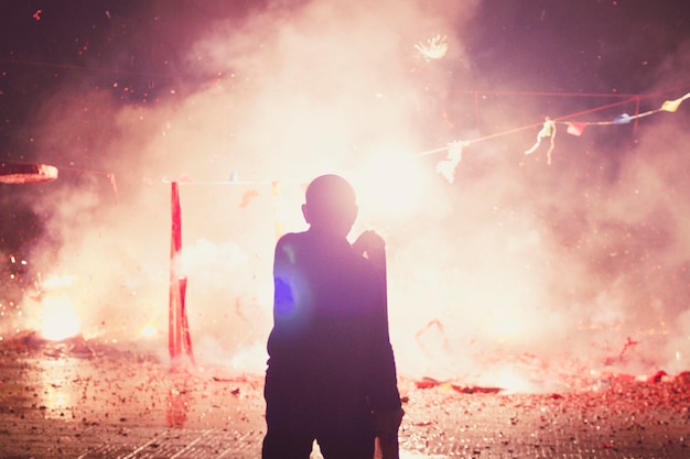 Foto vista traseira de um homem de pé junto a fogos de artifício na rua à noite