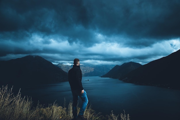 Foto vista traseira de um homem de pé na montanha ao lado do rio contra o céu nublado