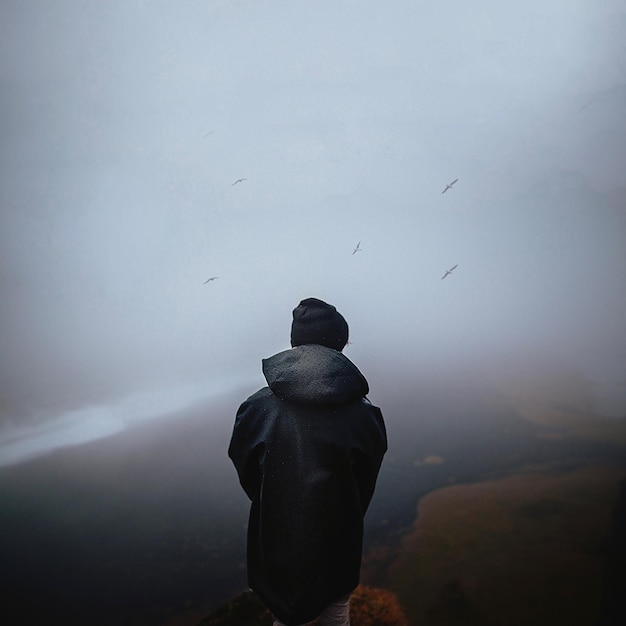 Vista traseira de um homem de pé na montanha contra o céu durante o tempo nebuloso