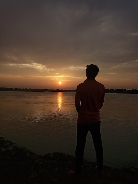 Foto vista traseira de um homem de pé na praia contra o céu durante o pôr do sol