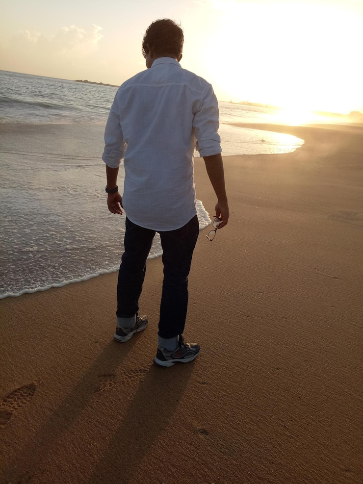 Foto vista traseira de um homem de pé na praia contra o céu durante o pôr do sol