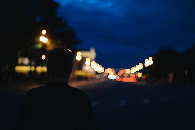 Foto vista traseira de um homem de pé na rua iluminada à noite