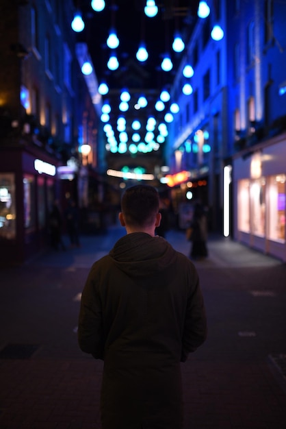 Foto vista traseira de um homem de pé na rua iluminada à noite