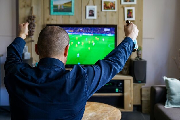 Foto vista traseira de um homem desfrutando de um jogo de futebol na televisão na sala de estar em casa