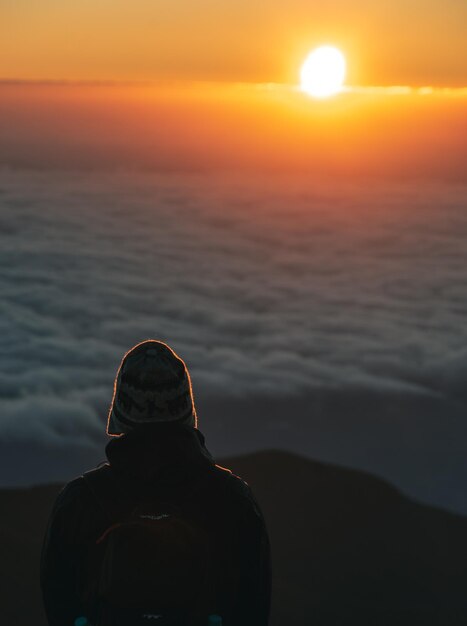 Foto vista traseira de um homem em silhueta olhando para o pôr do sol