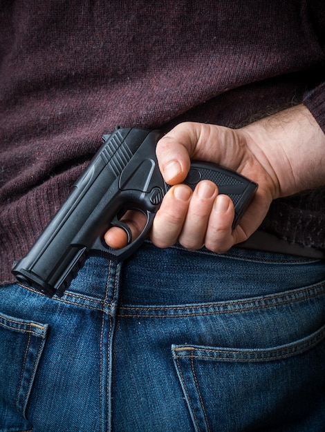 Vista traseira de um homem escondendo uma arma de brinquedo
