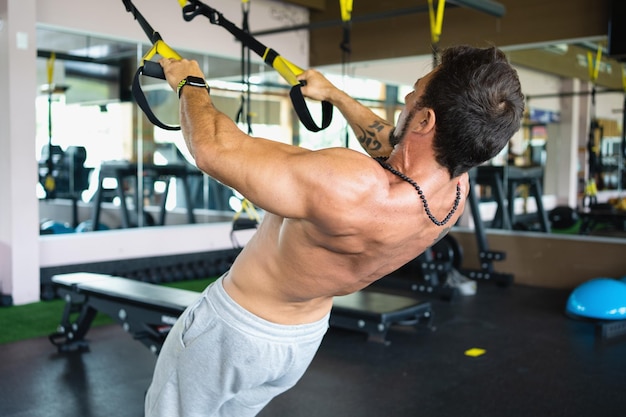 Vista traseira de um homem forte exercitando com trx