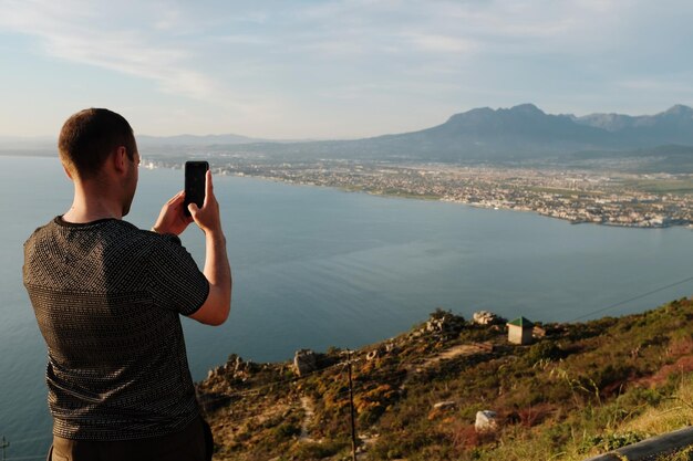 Vista traseira de um homem fotografando com telefone móvel contra o mar