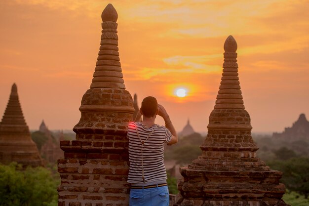 Foto vista traseira de um homem fotografando enquanto está de pé junto às estupas durante o pôr do sol