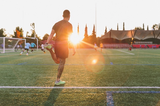 Vista traseira de um homem jogando futebol no campo durante o pôr do sol