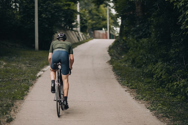 Vista traseira de um homem musculoso andando de bicicleta sozinho no parque verde