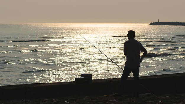 Foto vista traseira de um homem pescando na costa durante o pôr-do-sol