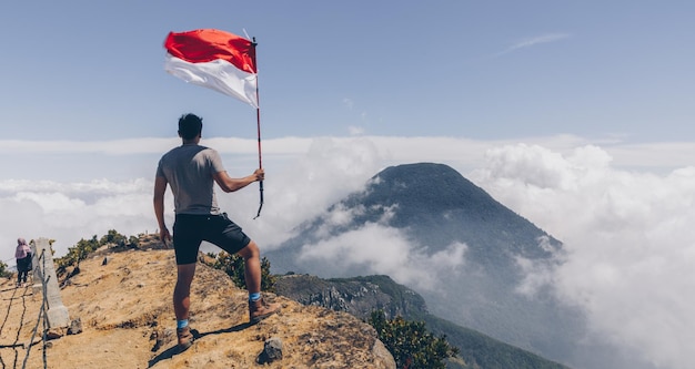 Vista traseira de um homem segurando uma bandeira enquanto está de pé na montanha contra o céu