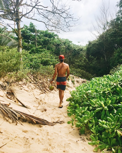 Foto vista traseira de um homem sem camisa caminhando na praia