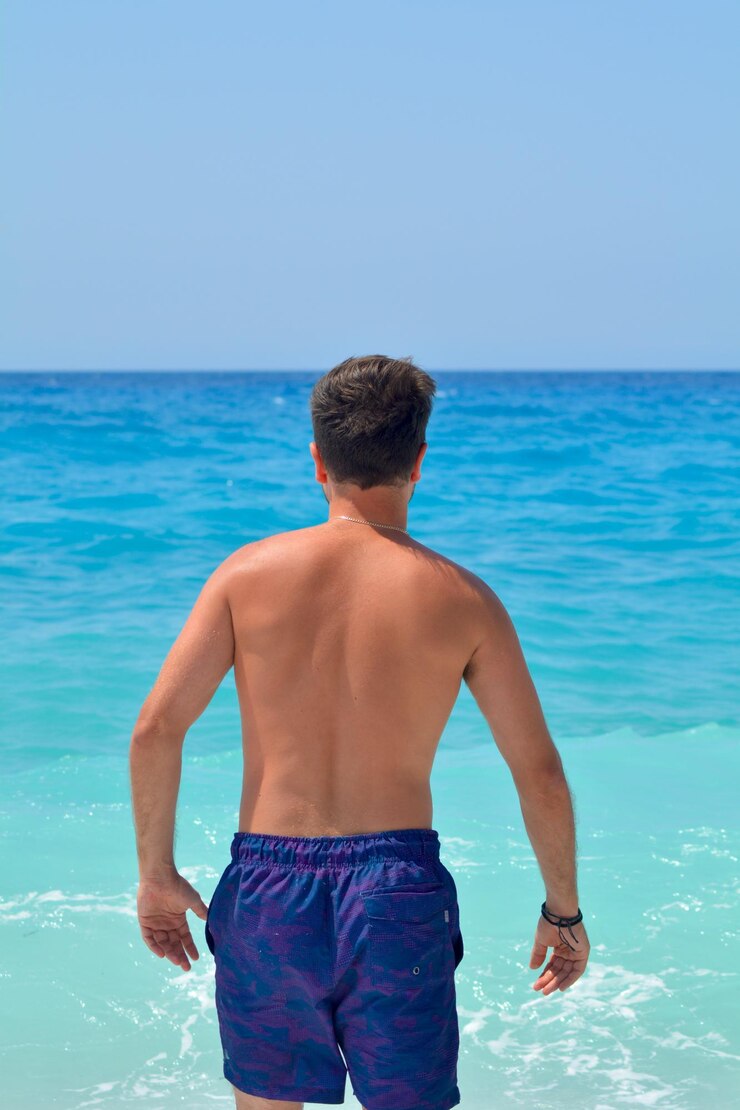 Foto vista traseira de um homem sem camisa de pé no mar contra o céu