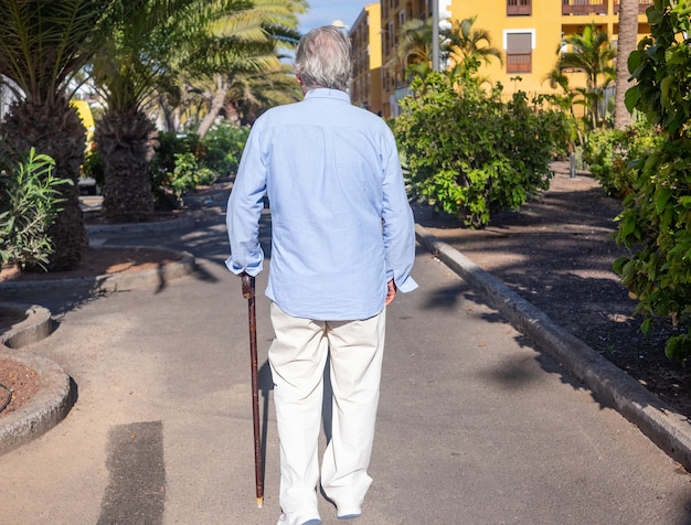 Vista traseira de um homem sênior com uma bengala caminhando ao ar livre em um dia ensolarado