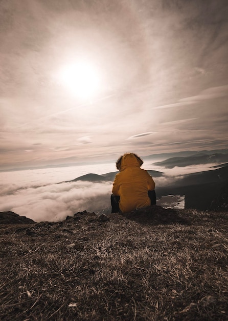 Foto vista traseira de um homem sentado na montanha contra o céu durante o pôr do sol