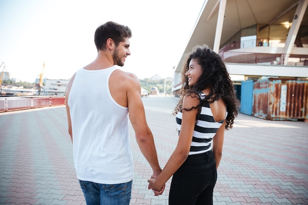 Vista traseira de um jovem casal alegre em pé e de mãos dadas ao ar livre