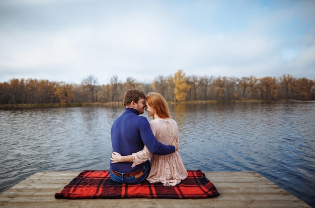 Vista traseira de um jovem casal romântico sentado no cais, apreciando a vista incrível