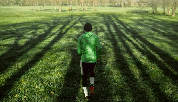 Foto vista traseira de um jovem corredor correndo na grama verde na floresta atlético masculino correndo no parque de manhã em um dia ensolarado estilo de vida saudável e conceito de esporte de pessoas