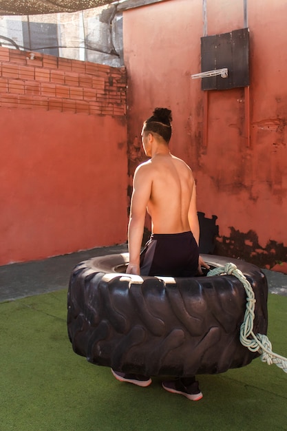 Vista traseira de um jovem homem musculoso, levantando e andando com uma roda de caminhão.