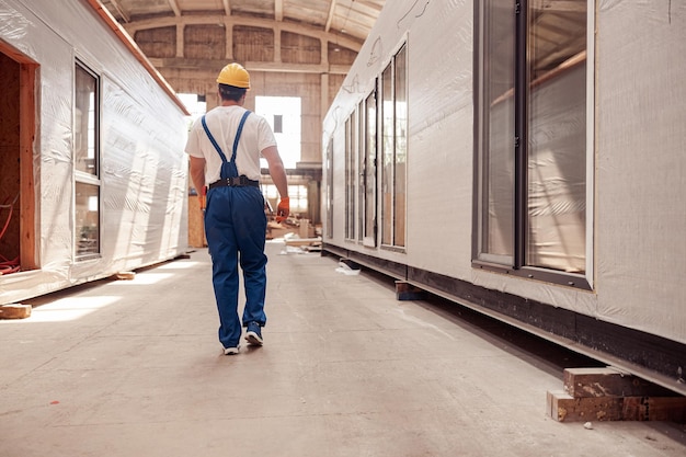 Vista traseira de um jovem trabalhador da construção civil caminhando entre duas casas de contêiner pré-fabricadas