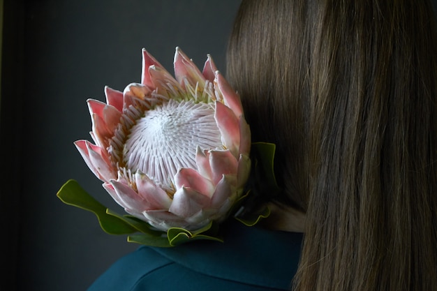 Vista traseira, de, um, menina, com, cabelo escuro, segurando, um, rosa protea, flor, ligado, um, fundo escuro, foco seletivo