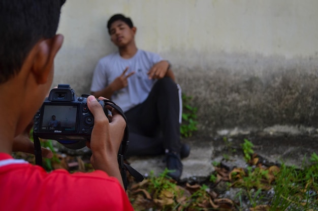 Foto vista traseira de um menino adolescente fotografando um amigo sentado contra a parede