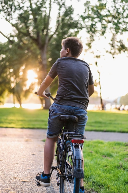 Foto vista traseira de um menino andando de bicicleta na estrada