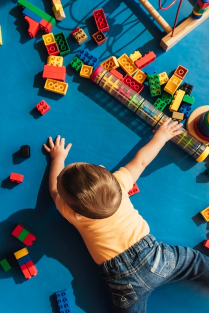 Vista traseira de um menino brincando com brinquedos enquanto está deitado no chão em casa