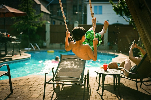 Foto vista traseira de um menino brincando de balanço à beira da piscina