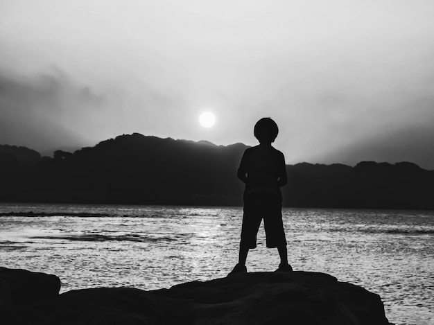 Foto vista traseira de um menino de pé em uma rocha contra o mar