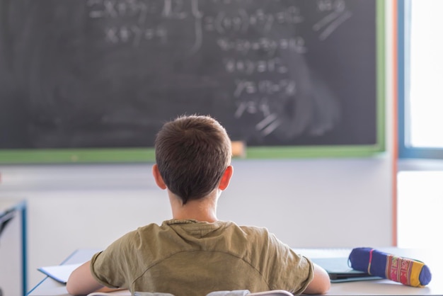 Vista traseira de um menino sentado na sala de aula