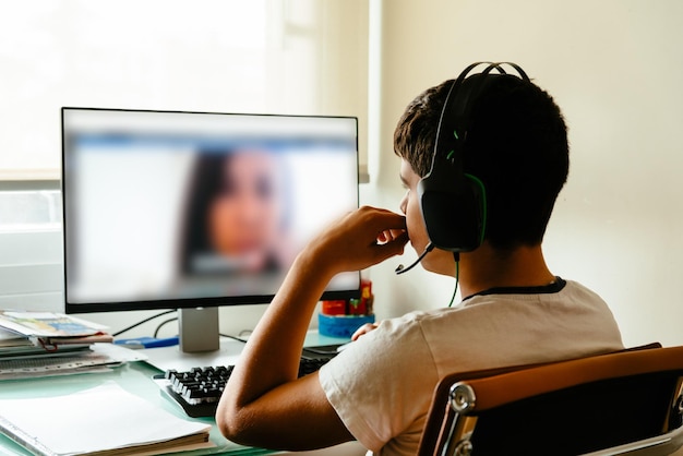 Vista traseira de um menino usando o computador enquanto está sentado à mesa