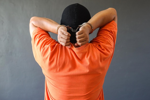 Vista traseira de um prisioneiro em camiseta laranja usando algema isolada sobre fundo cinza