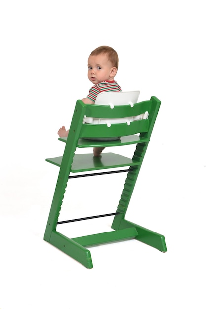 Vista traseira de um retrato completo de um bebê sentado em uma cadeira olhando para a câmera no fundo branco