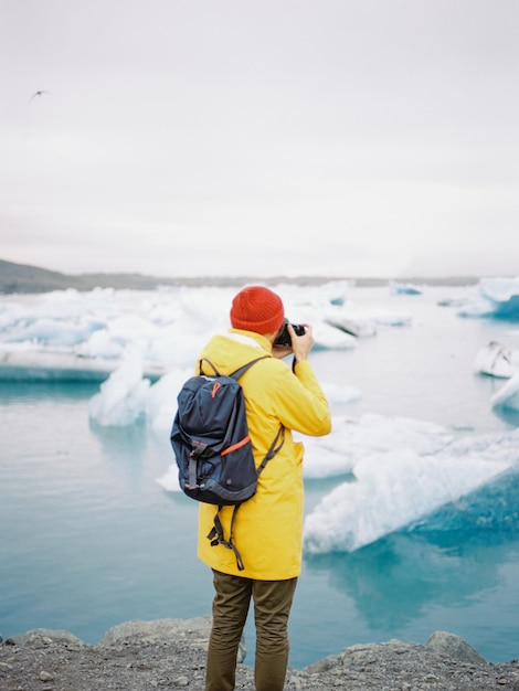 Foto vista traseira de um turista fotografando uma geleira no lago durante o inverno