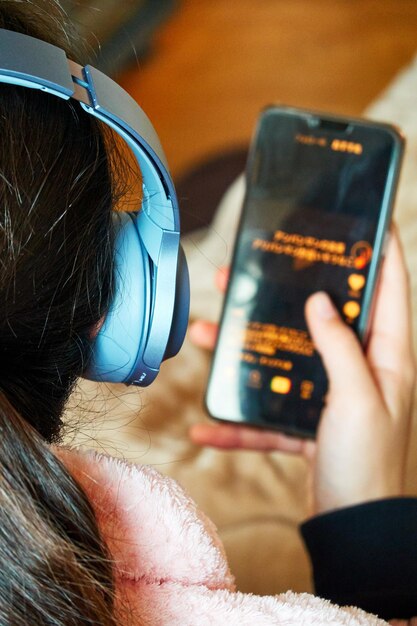 Foto vista traseira de uma adolescente usando um telefone móvel com fones de ouvido