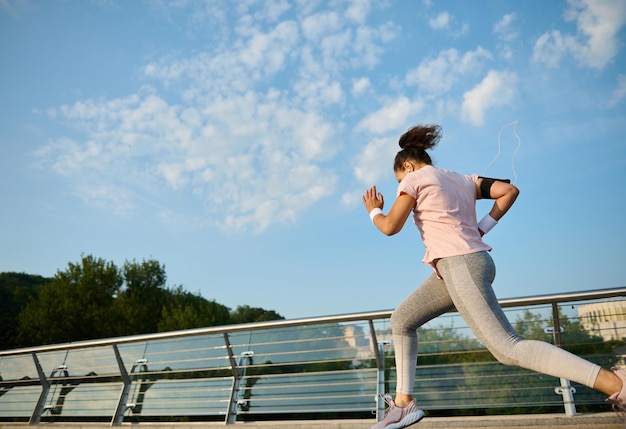 Vista traseira de uma determinada mulher ativa correndo em uma esteira sobre a ponte da cidade. Esporte, fitness, estilo de vida saudável e conceito de perda de peso